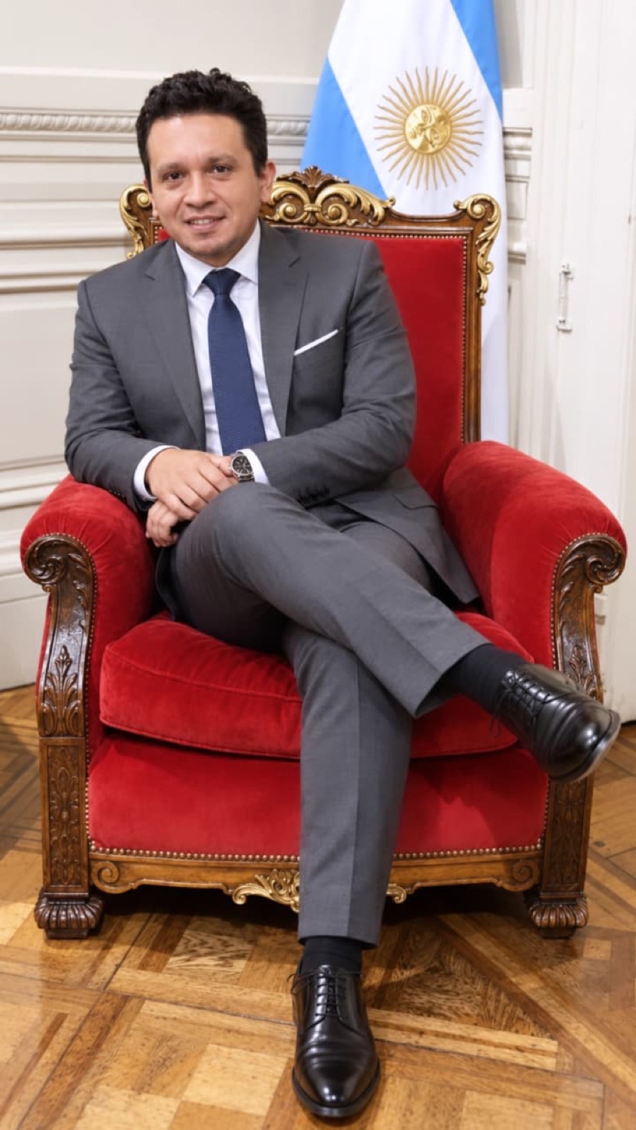 Diego Macana Roa sentado en un sillón rojo junto a la bandera argentina